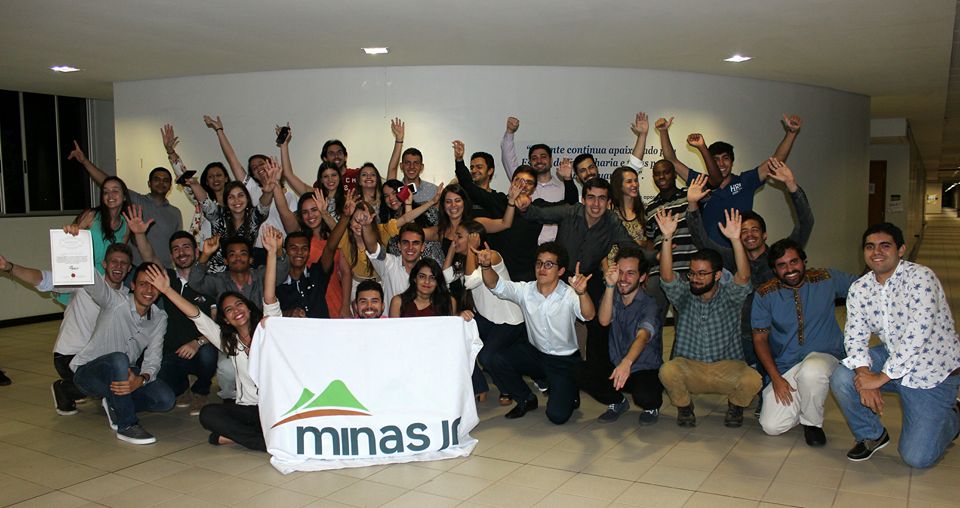 grupo de jovens reunidas comemorando com os braços levantados para cima segurando uma bandeira.