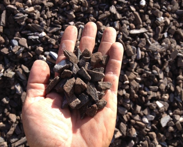 mão segurando fragmentos de formato irregular de minério de ferro 