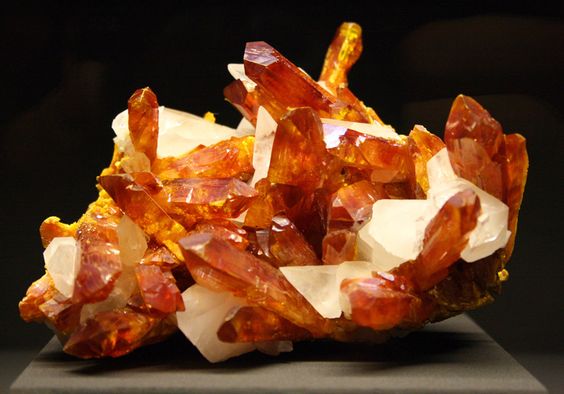 Imagem mostrando uma drusa (contem vários cristais de minerais) com cristais laranjas e brancos de Auripigmento 