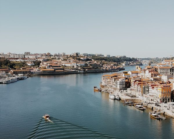A imagem mostra uma cidade em Portugal, com um rio passando entre ela. Há alguns barcos e casas coloridas e próximas.