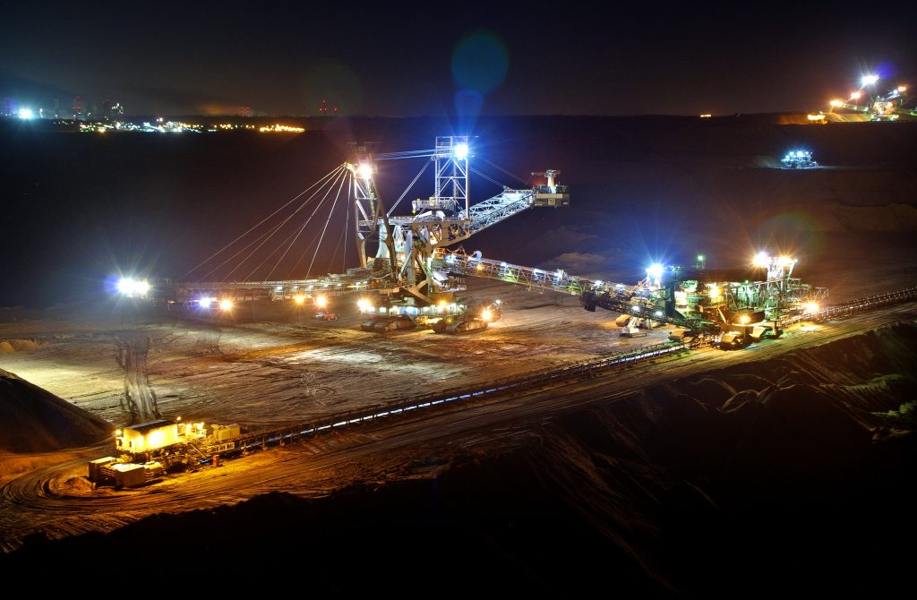 Imagem mostrando um grande guindaste e escavadeiras, todos utilizados para extrair carvão. Está de noite e existem luzes acesas nas máquinas.