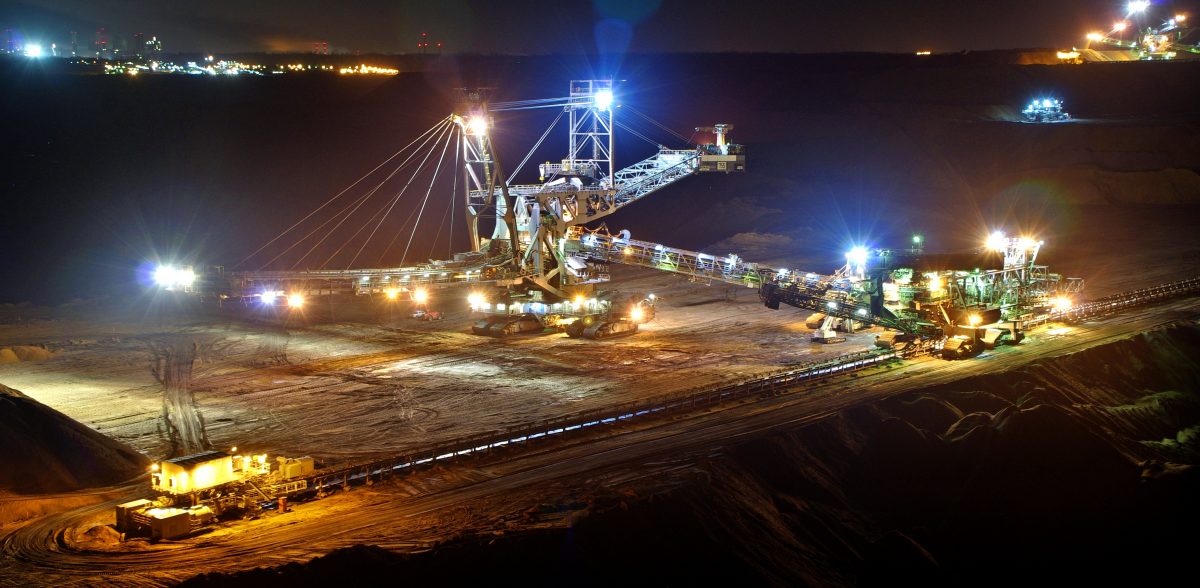 Imagem mostrando um grande guindaste e escavadeiras, todos utilizados para extrair carvão. Está de noite e existem luzes acesas nas máquinas.