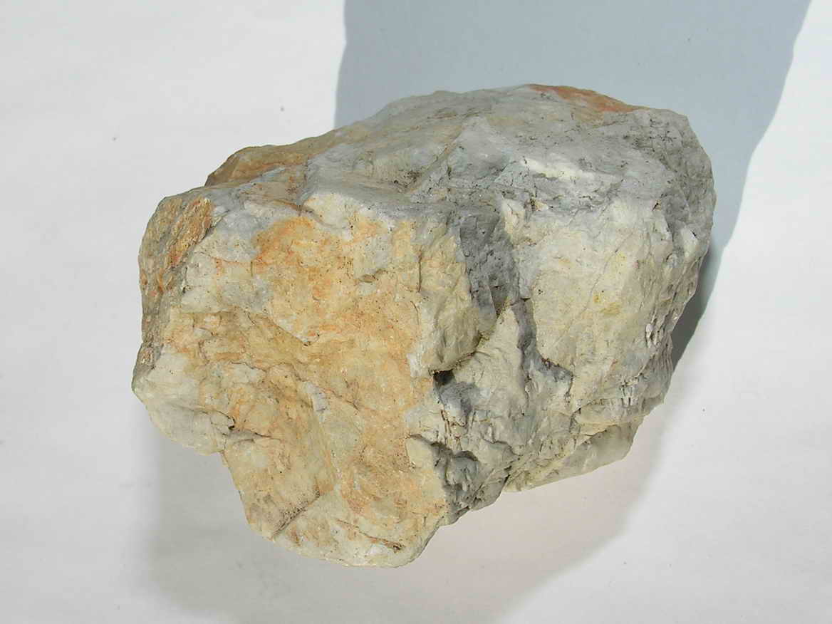 Foto mostrando um mineral branco, com manchas. Ele tem forma irregular.