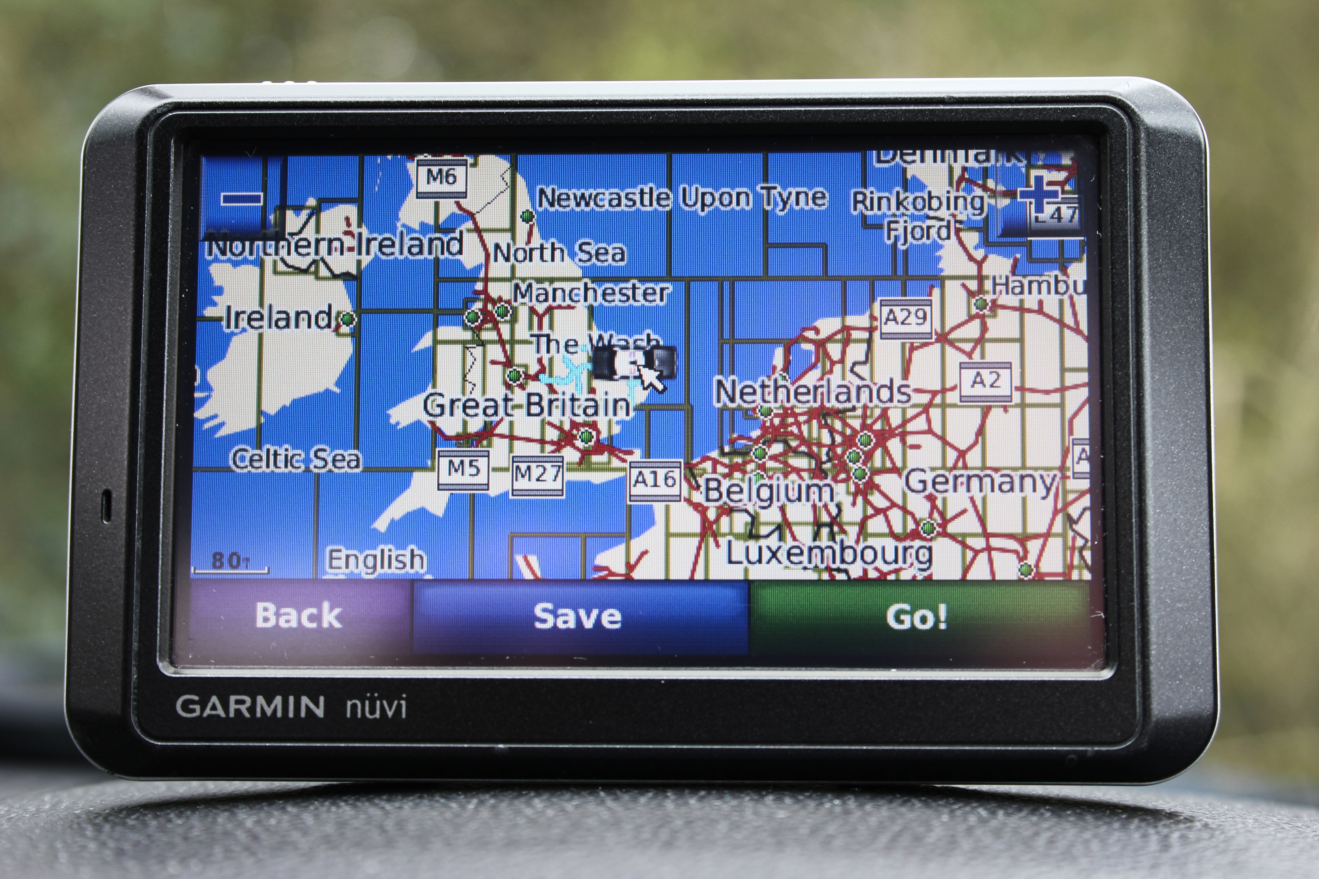 Foto mostrando um dispositivo GPS no centro dela, em um carro. O GPS está ligado e tem um mapa aparecendo.