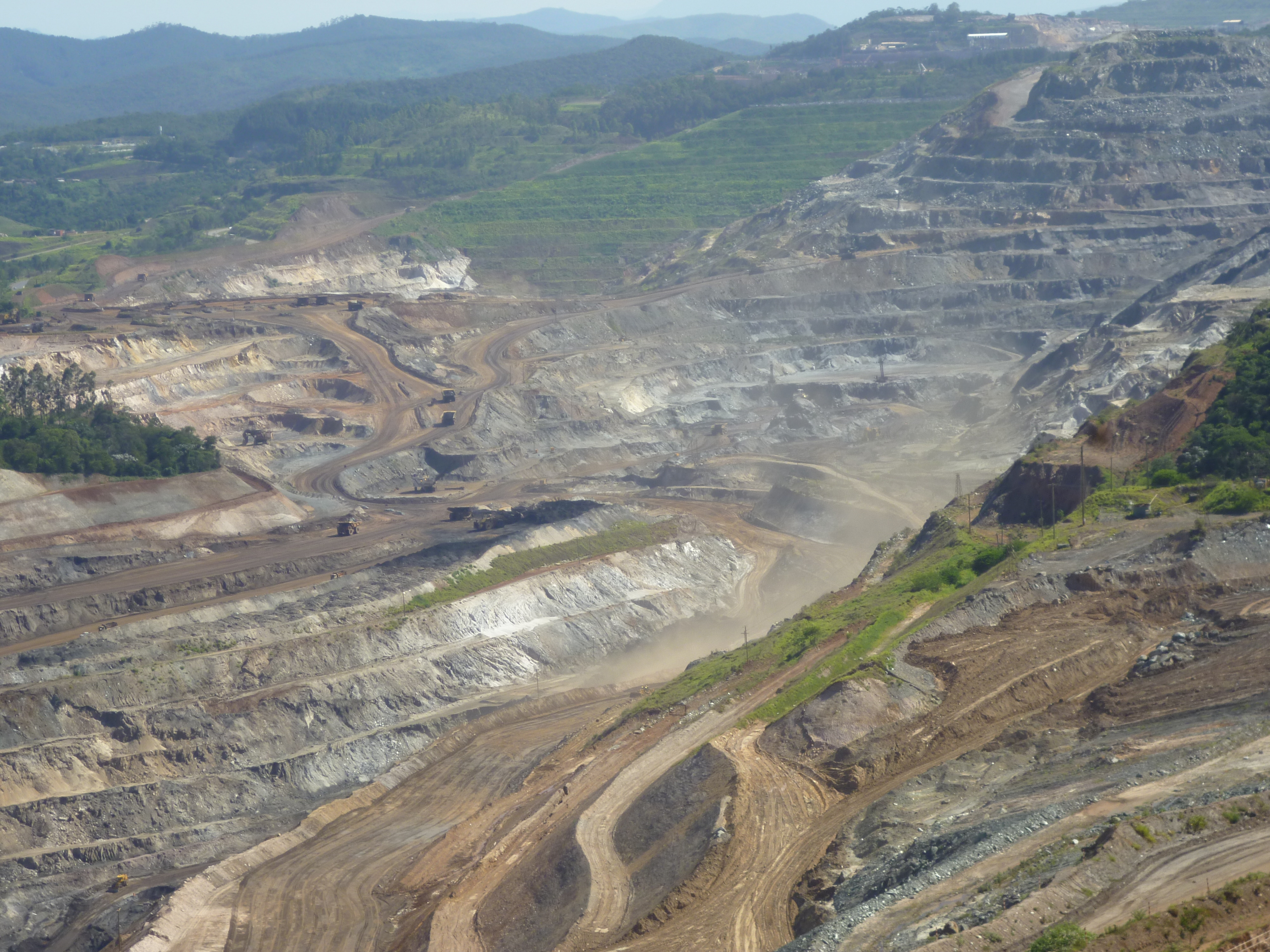 Foto mostrando a cava de uma mina em Itabira, ela possui curvas que variam em tons de marrom e cinza.