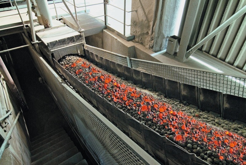 Na foto, há um tubo cilíndrico cortado ao meio, por ponde passam várias pedras (clínquer) superaquecidas e de cor avermelhada, para resfriar até poder moer e produzir o cimento.